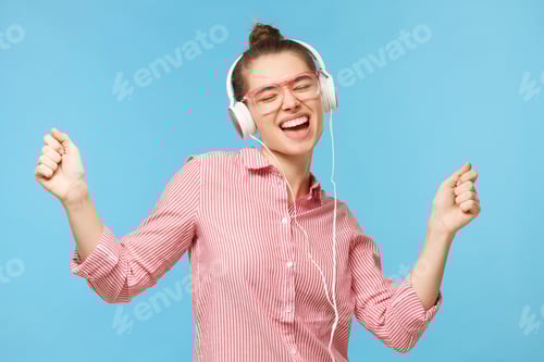 Preview: Young smiling woman wearing pink glasses, listening to music through headphones, dancing