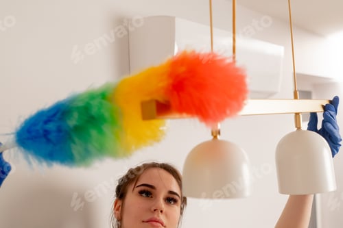 Preview: close up in the apartment cleaning lady in a yellow apron is cleaning a chandelier with a dust brush