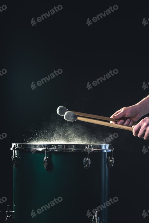 Preview: A man plays a musical percussion instrument with sticks on a dark background.