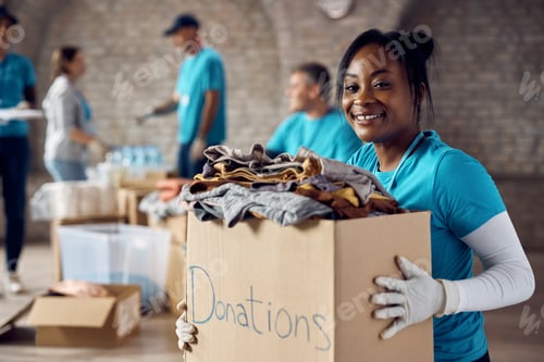Preview: Happy African American woman volunteering at humanitarian aid center and looking at camera.