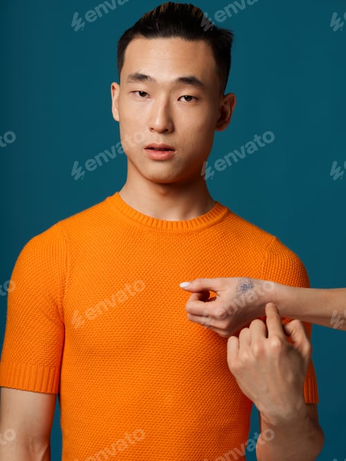 Preview: Asian man in orange t-shirt on blue background gesturing with hands cropped view