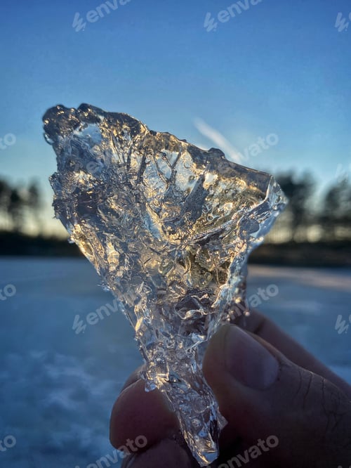 Preview: piece of ice in hand against the backdrop of the setting sun. rays of the sun in a piece of ice