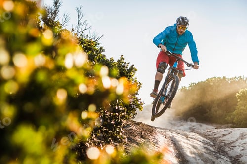 Preview: Cyclist catching air on a mountain bike trail at sunset.