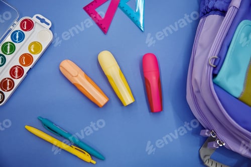Visualização: Mochila com material escolar colorido plana sobre fundo azul