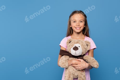 Preview: Smiling child holding teddy bear isolated on blue