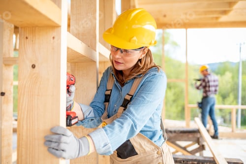 Preview: Female worker at construction site during work with wood frame house