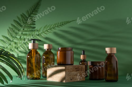 Preview: Bottles for cosmetics and cream on a pedestal, green background with leaves and shadow. Brown glass