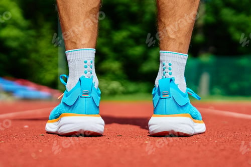 Preview: Athlete Wearing Bright Blue Running Shoes on Red Stadium Track During Training