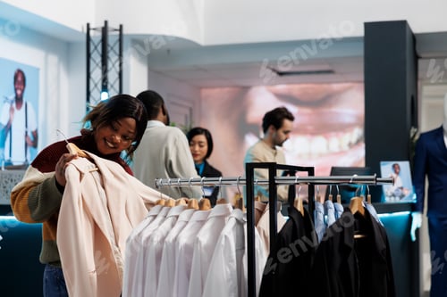 Preview: Woman holding outfit to body in boutique