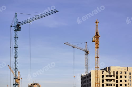 Preview: Working tall cranes inside place for with tall buildings under construction against a clear blue sky