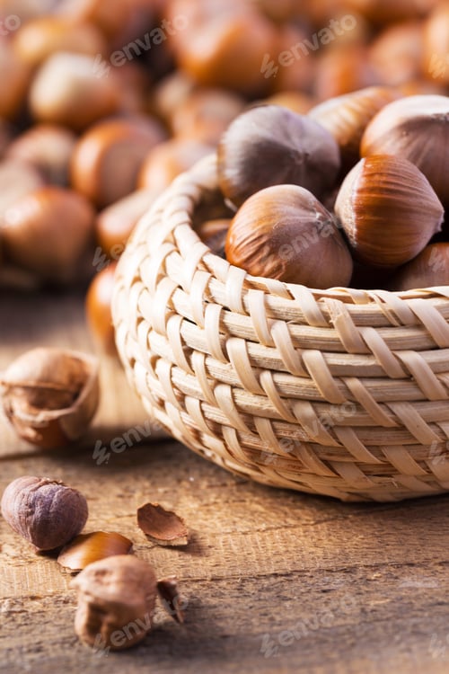 Preview: Hazelnuts in a woven basket on a wooden surface with scattered nuts around