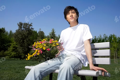 Preview: Young Man Sitting On A Park Bench Holding Flowers