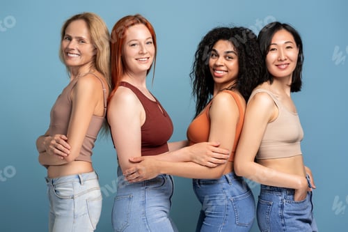 Preview: Diverse group of women wearing stylish tops embracing on blue background, looking at camera