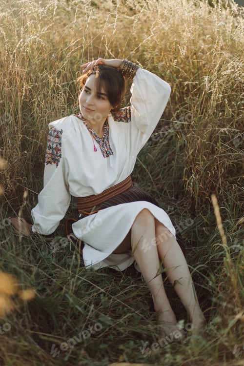 Preview: Young woman in traditional national embroidered shirt and skirt on nature at sunset.