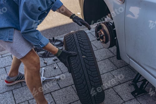 Preview: Young man changing a car tire on the road, using a wrench to unscrew the lug nuts