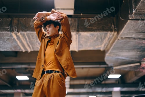 Preview: Stylish young man in brown suit stretching in urban setting