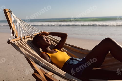 Preview: Side view of young African-american woman relaxing in a hammock on the beach