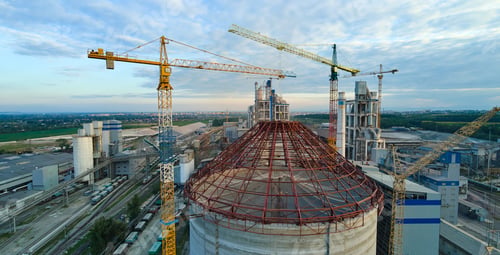 Preview: Aerial view of cement factory under construction with high concrete plant structure and tower cranes