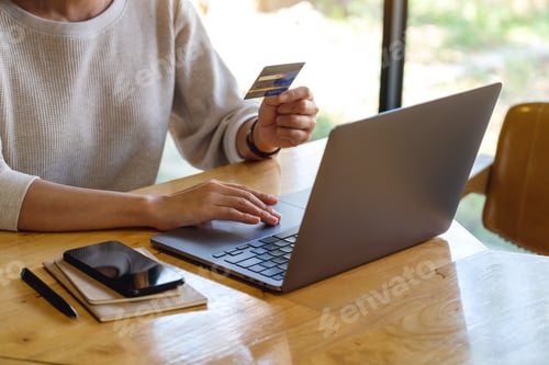 Preview: Closeup image of a woman holding credit cards while using laptop computer in office