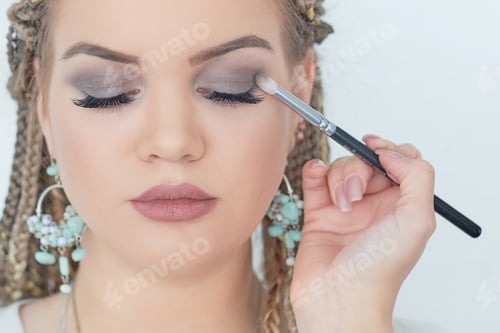 Preview: Professional makeup artist working with beautiful young woman. bright blonde model