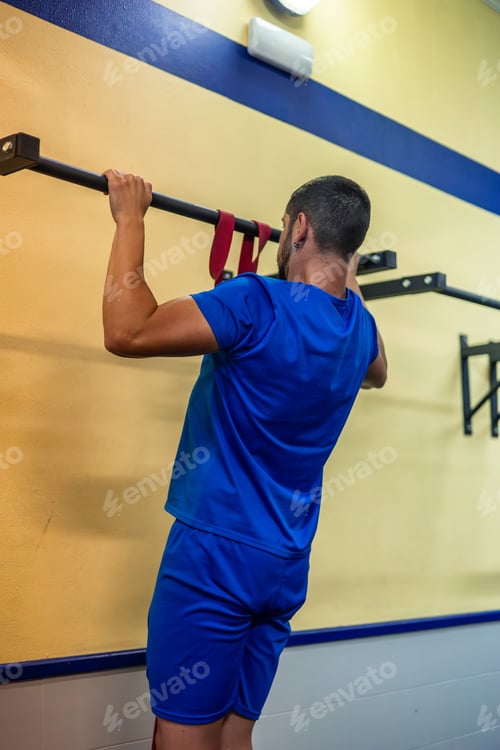 Preview: young fitness sportsman doing pull-ups to train back muscles on calisthenics bar in gym