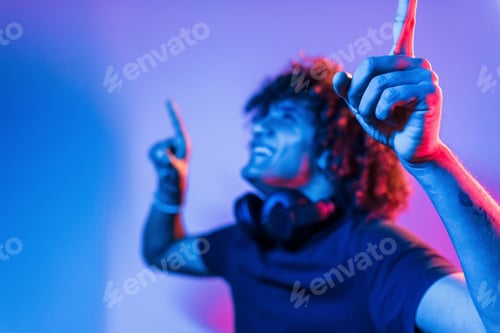 Vista previa: With headphones. Young beautiful man with curly hair is indoors in the studio with neon lighting