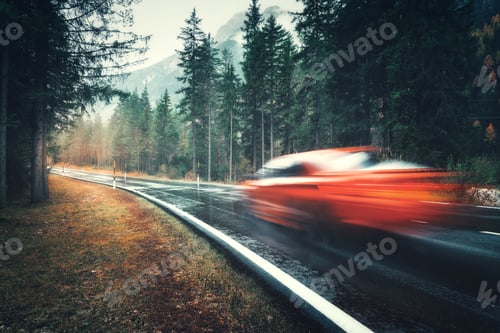 Preview: Blurred red car in motion on the road in autumn forest