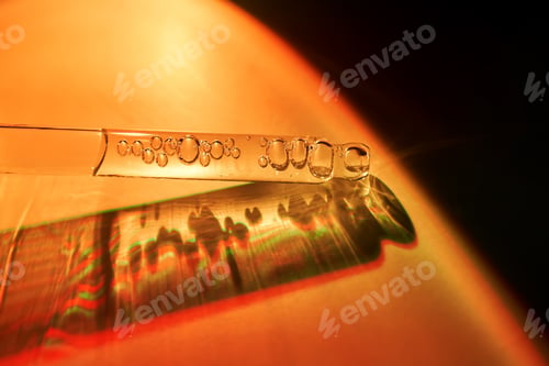 Preview: A dropper with sunscreen body serum in the orange sunset light.