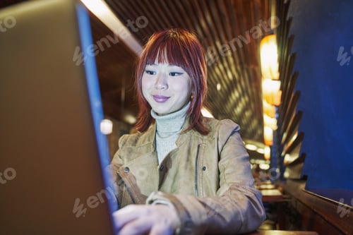 Preview: young asian woman using her laptop computer sitting at a table in a coffee shop