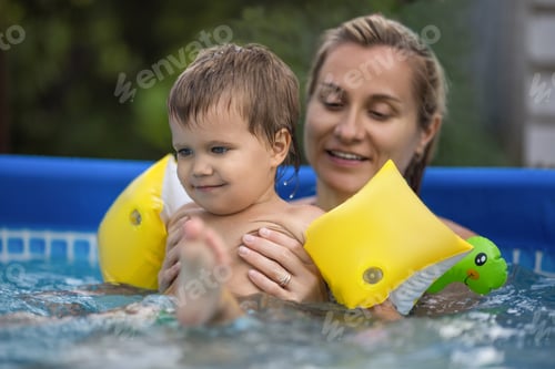 Preview: Mom plays with a naked baby in oversleeves in the pool against the background of a summer sunset