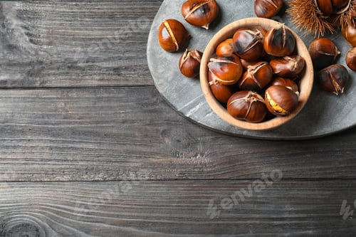 Preview: Delicious roasted edible chestnuts on black wooden table, top view. Space for text