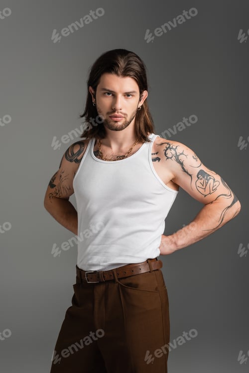 Preview: Tattooed model in pants and white tank top isolated on grey