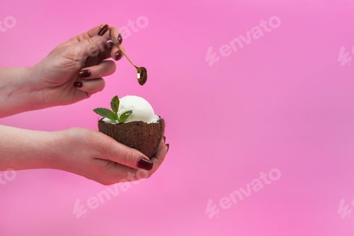 Preview: Vanilla ice cream balls in a fresh coconut half, decorated with mint leaves in the hand with a spoon
