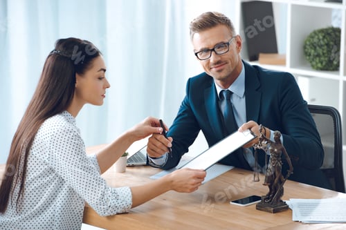 Preview: handsome lawyer smiling at camera while giving clipboard with document and pen to female client