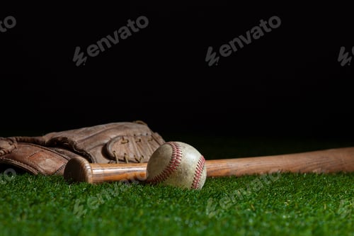 Preview: Old baseball bat and mitt low angle on grass field and dark background