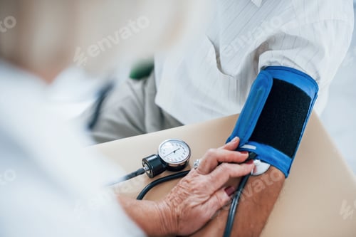 Preview: Close up view. Female doctor uses tonometer to make blood pressure measuring to senior man