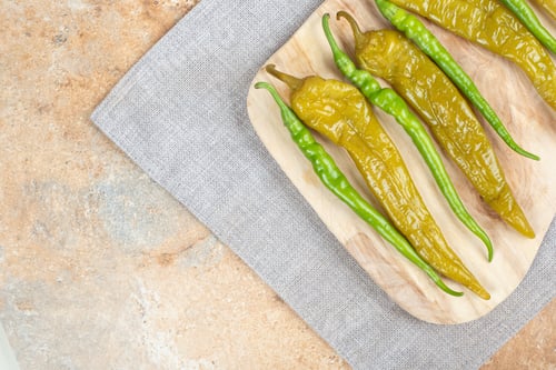 Preview: Pickled and fresh green peppers on wooden board