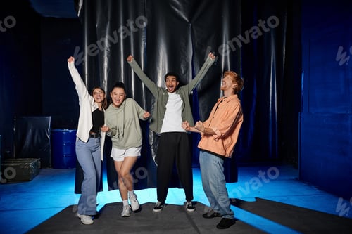 Preview: group of young multicultural friends celebrating success in an escape room challenge, rejoice