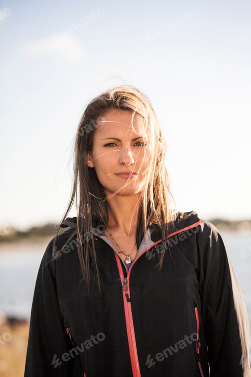 Preview: Portrait of woman in jacket standing by lake against sky on sunny day