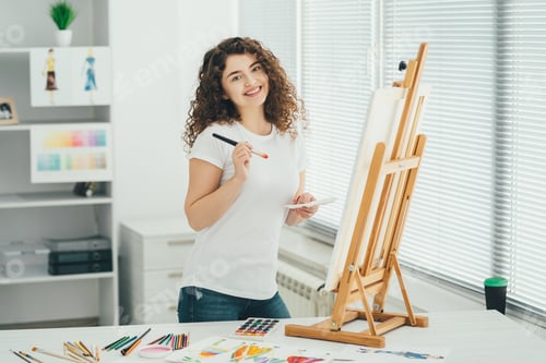 Preview: The cute woman with an art brush painting a picture on the easel.