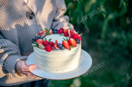 Preview: Unrecognizable girl holding white tasty cake decorated with fresh berries. Natural light and shadow