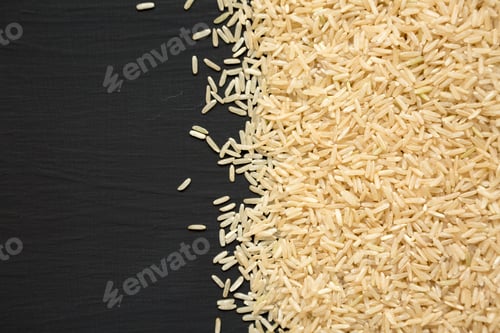 Vista previa: Dry Brown Rice on a black surface, top view. Overhead, from above, flat lay. Space for text.