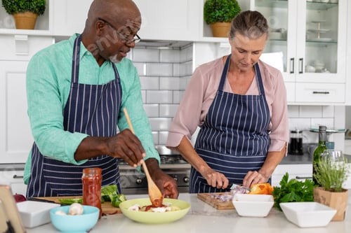 Preview: Senior multiracial couple preparing food together in kitchen at home