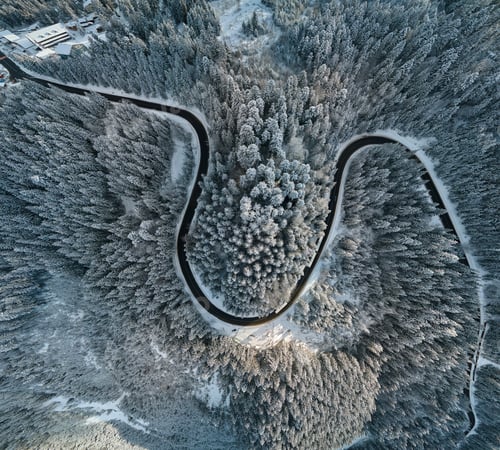 Preview: Aerial view of winter landscape with snow covered mountain hills and winding forest road in morning.