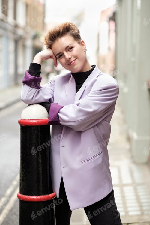 Preview: Natural portrait of short-hair young woman leaning on bollard in the street.