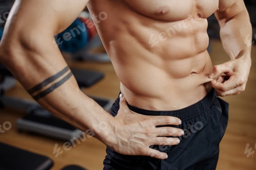 Preview: Muscular athletic young man bodybuilder fitness model measuring fat percent in gym. Perfect abs.