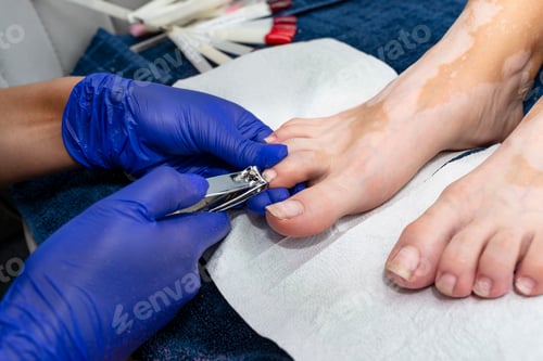 Preview: The manicurist cuts her toenails with a nail clipper wearing blue latex gloves.