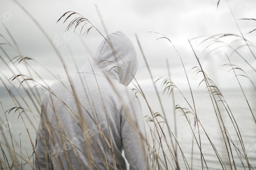 Preview: A lonely sad person from behind with a hoodie sitting near the sea thinking about life