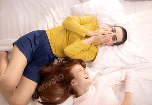 Preview: Top view of two women lying on a bed and talking closely