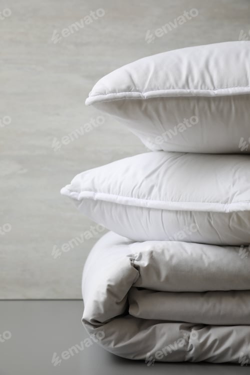 Preview: Soft folded blanket and pillows on light grey table, closeup